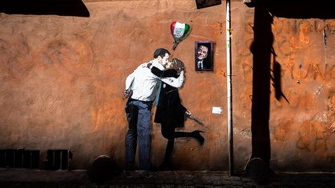 Stencil Graffiti an einer Hauswand: ein Paar küsst sich, daneben schaut Berlusconi aus einem Fenster