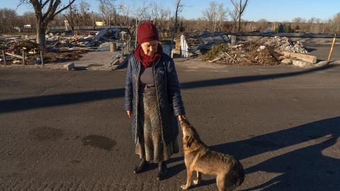 Wera Larina steht vor zerstörten Gebäuden und streichelt einen Hund