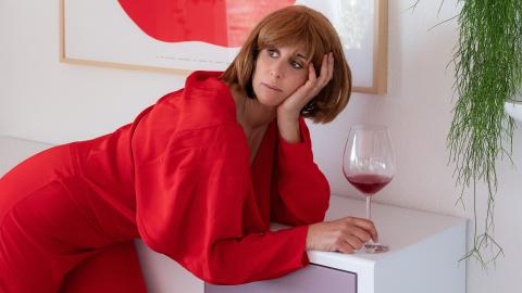 Selbstportrait-Inszenierung von Nora Rupp: Sie steht vor einem Gemälde eines Apfels und  schaut mit gedrehtem Kopf ins Leere, daneben steht ein Glas Wein