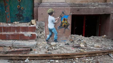 Graffiti an einer Hauswand: ein Junge schlägt mit einem Hammer ein Loch in die Wand, durch das Loch wachsen Sonnenblumen