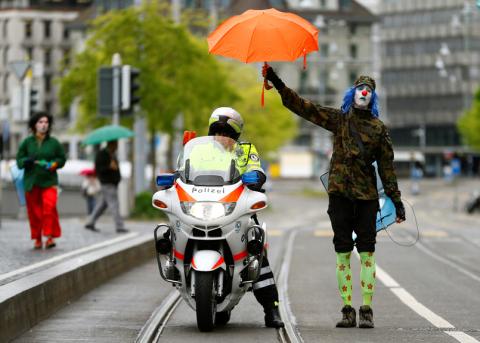 Clown-Aktivist mit Regenschirm begleitet ein Polizei-Motorrad
