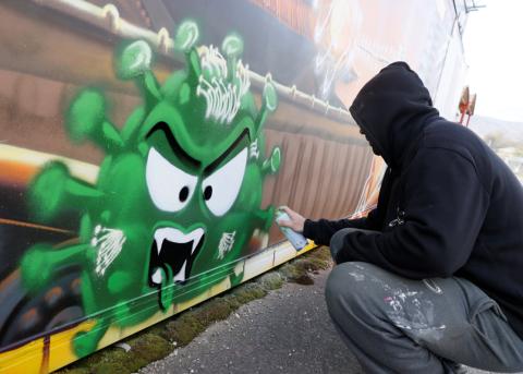Person sprayt ein Graffito eines Virus an eine Wand