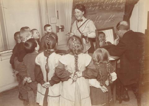 Gehörlose Kinder mit den Händen hinter dem Rücken schauen zur Lehrerin