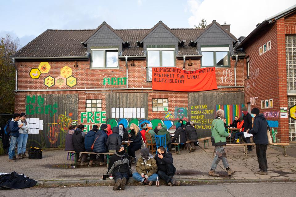 Personen sitzen vor einem Gebäude in Luetzerath welches mit Bannern behängt ist