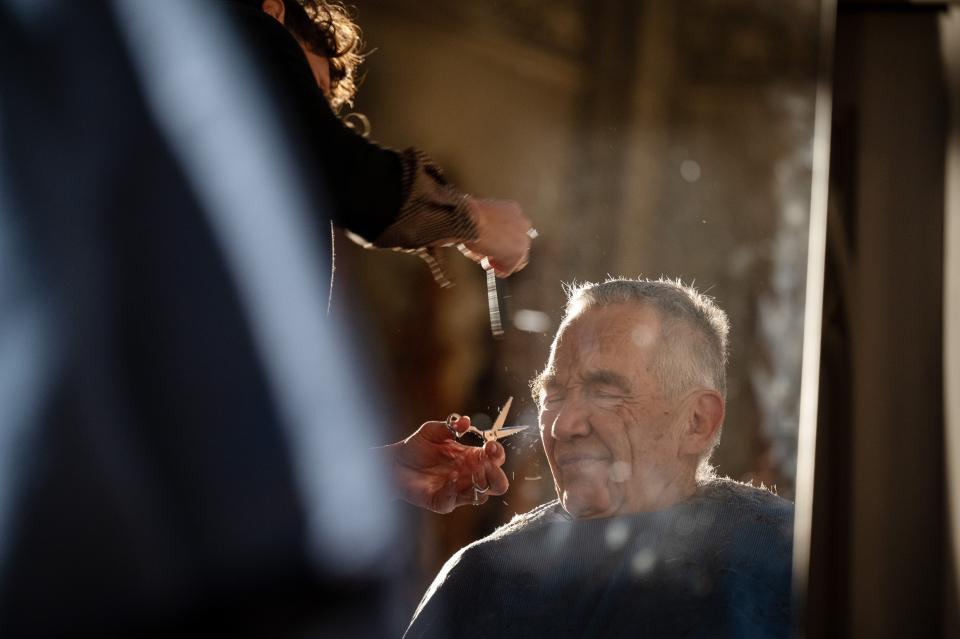 Anna Tschannen schneidet einem älteren Mann die Haare, welcher die Augen zukneift