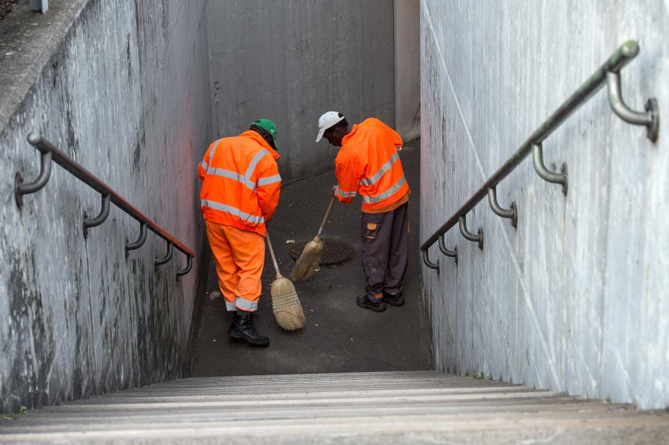 zwei Asylsuchende in oranger Arbeitskleidung reinigen eine Treppe